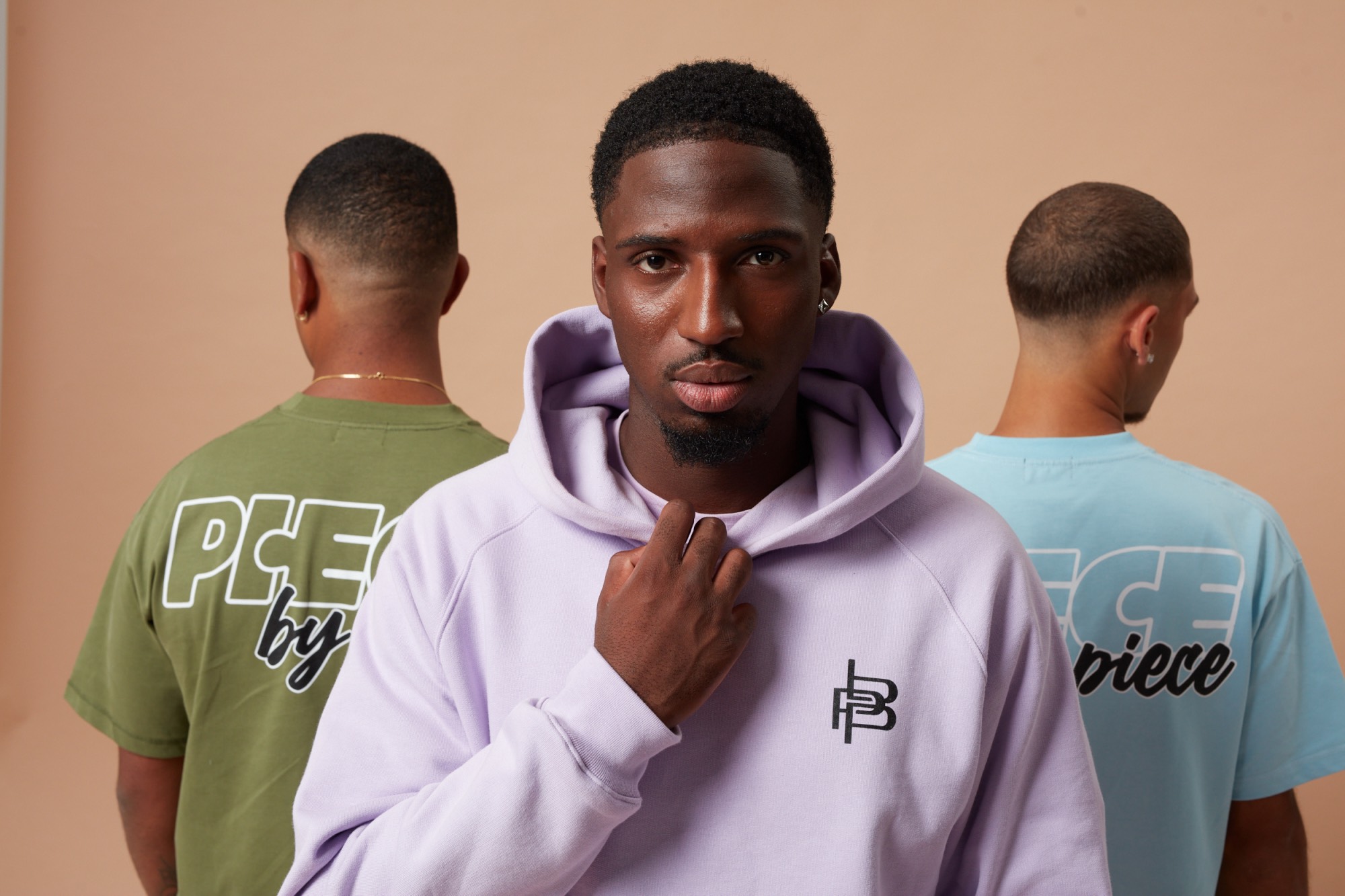 Drei Models in fliederfarbenem Hoodie sowie olivgrünem und hellblauem T-Shirt von Piece by Piece
